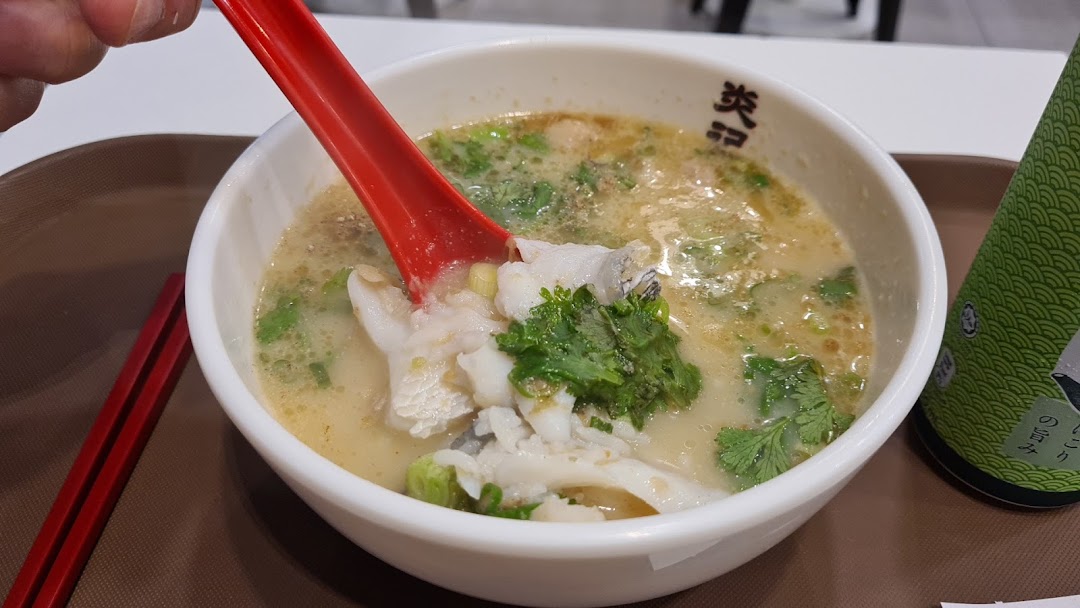 A close-up of a bowl of Yan Ji Gourmet Seafood Soup with fish slices, cilantro, and a red spoon.