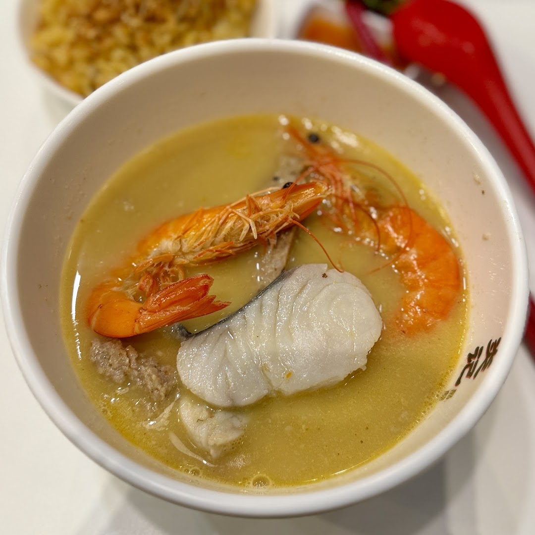 A close-up of a delicious bowl of seafood soup with prawns, fish, and minced meat in a rich broth.