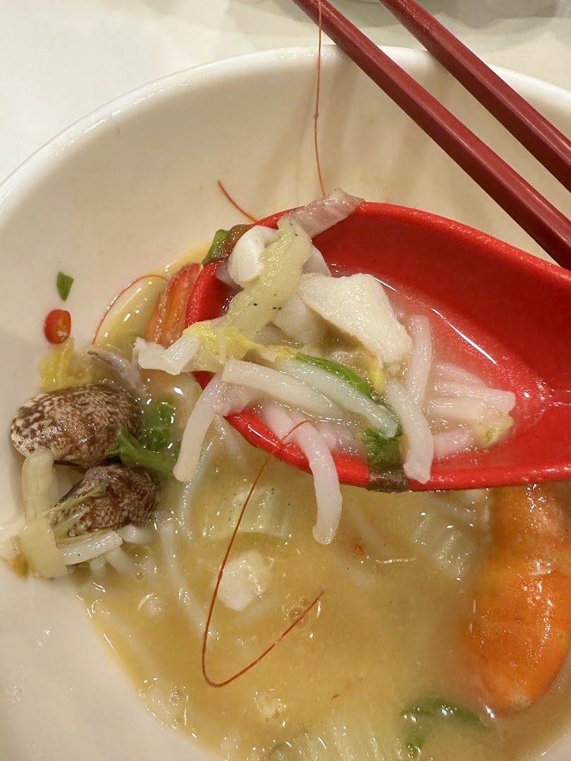 A close-up of a spoonful of gourmet seafood soup with noodles, vegetables, and seafood.