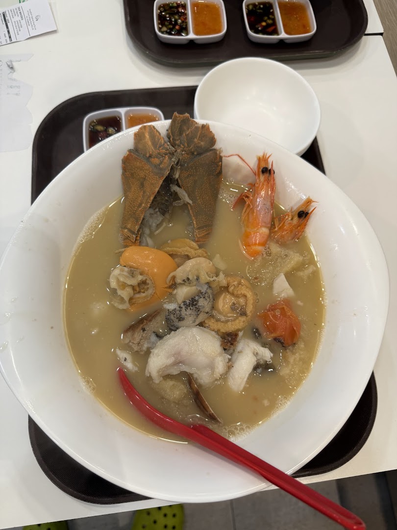A large bowl of rich seafood soup featuring mantis shrimp, prawns, abalone, and fish, served with dipping sauces.
