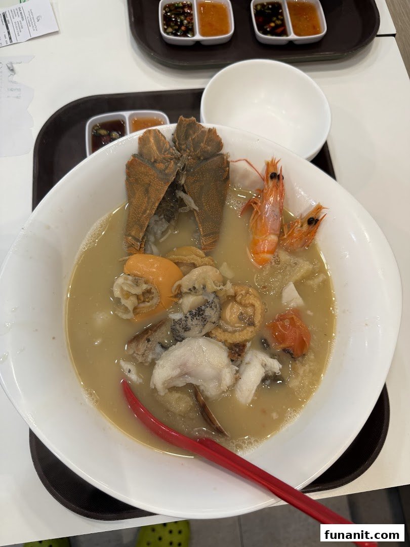 A large bowl of rich seafood soup featuring mantis shrimp, prawns, abalone, and fish, served with dipping sauces.