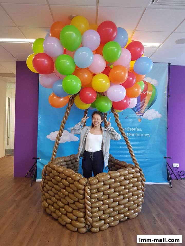 A woman poses in a balloon hot air balloon basket with colorful balloons.
