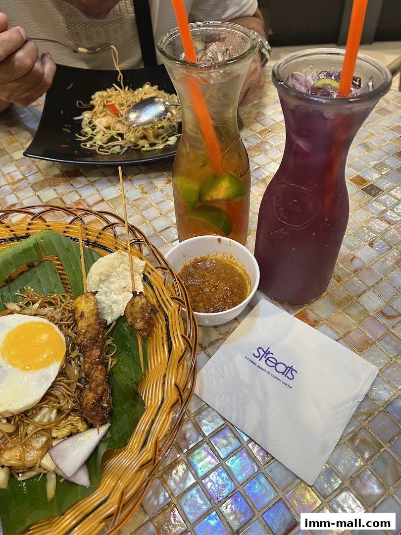 A close-up of a meal with noodles, satay, fried egg, and drinks.