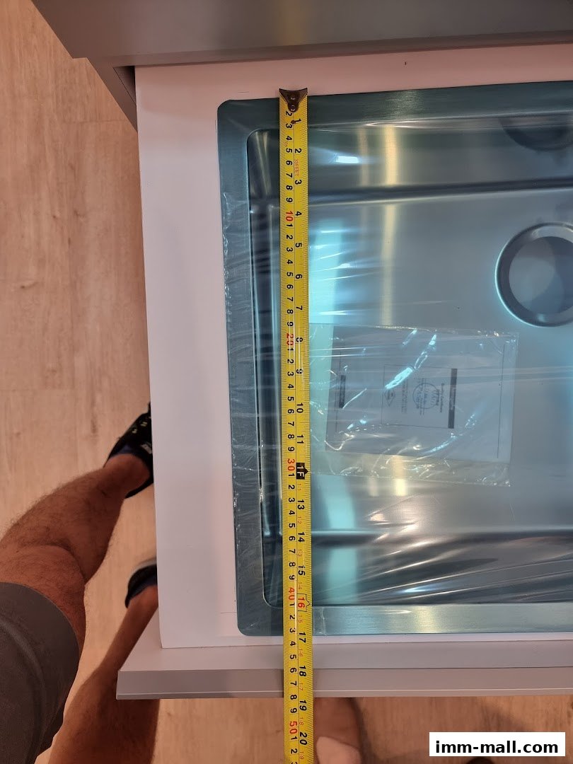 A person is measuring a stainless steel sink with a tape measure.
