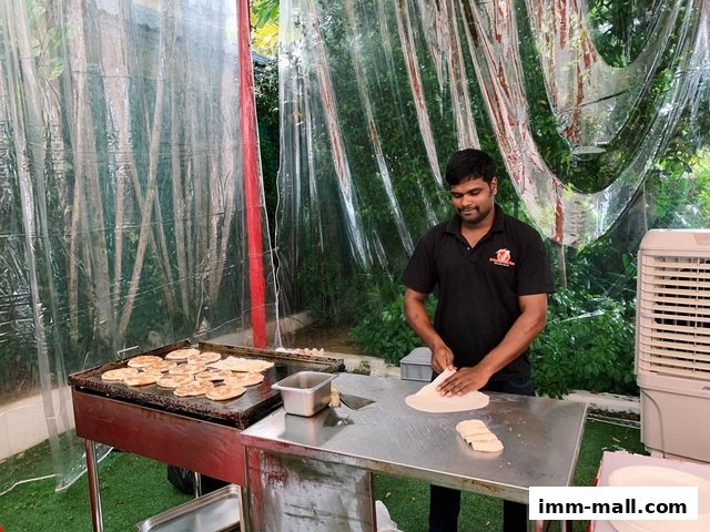 A man prepares dough in front of a griddle with food cooking.