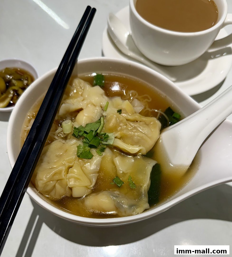 A bowl of wonton noodle soup with chopsticks and a cup of tea.