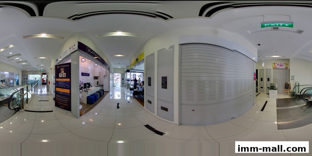 A panoramic view of a shopping mall corridor with shops and escalators.