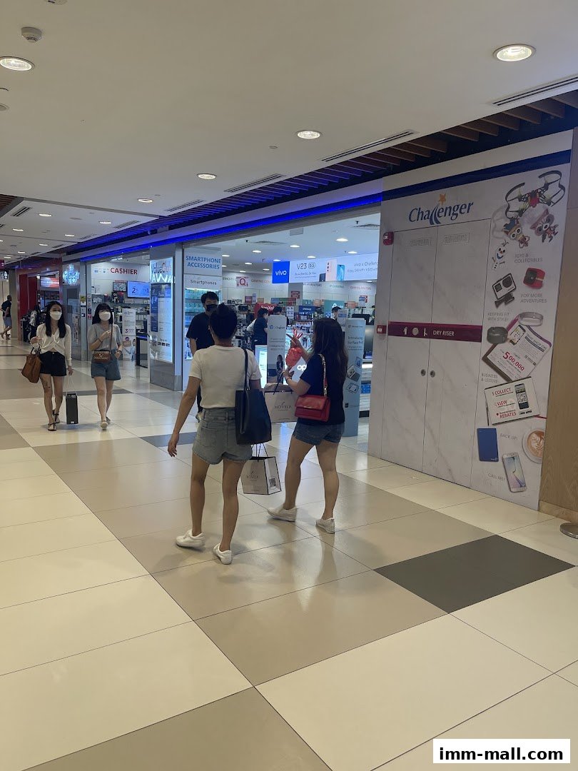 People walking past a Challenger electronics store in a mall, showcasing various products.