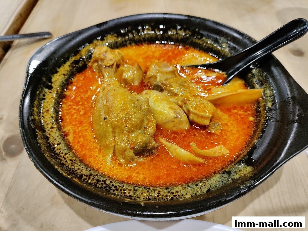 A close-up shot of a delicious bowl of curry chicken with potatoes and a spoon.