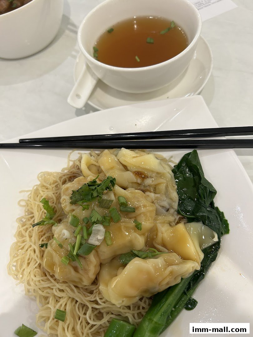 A close-up of wonton noodles with broth and greens, garnished with chopped scallions.