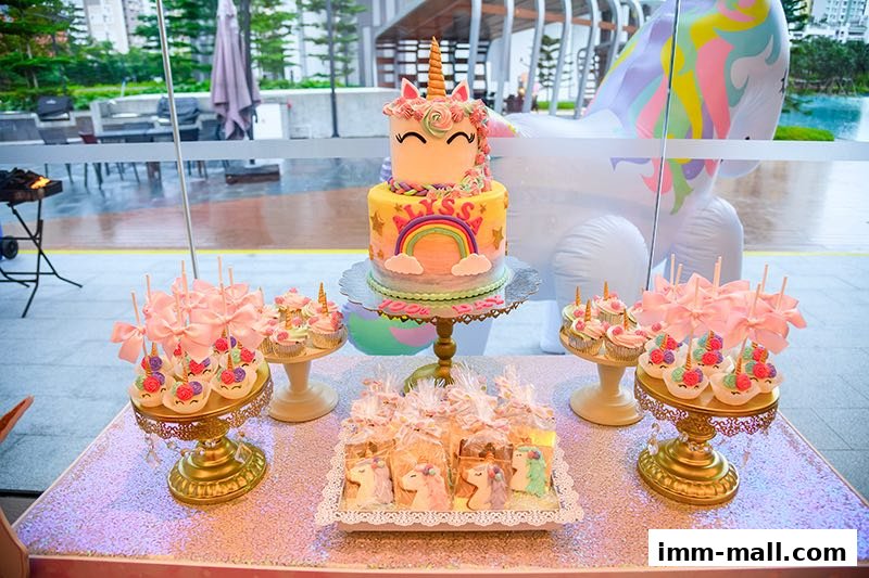 A beautifully decorated dessert table featuring a unicorn cake, cupcakes, and cookies for a party.