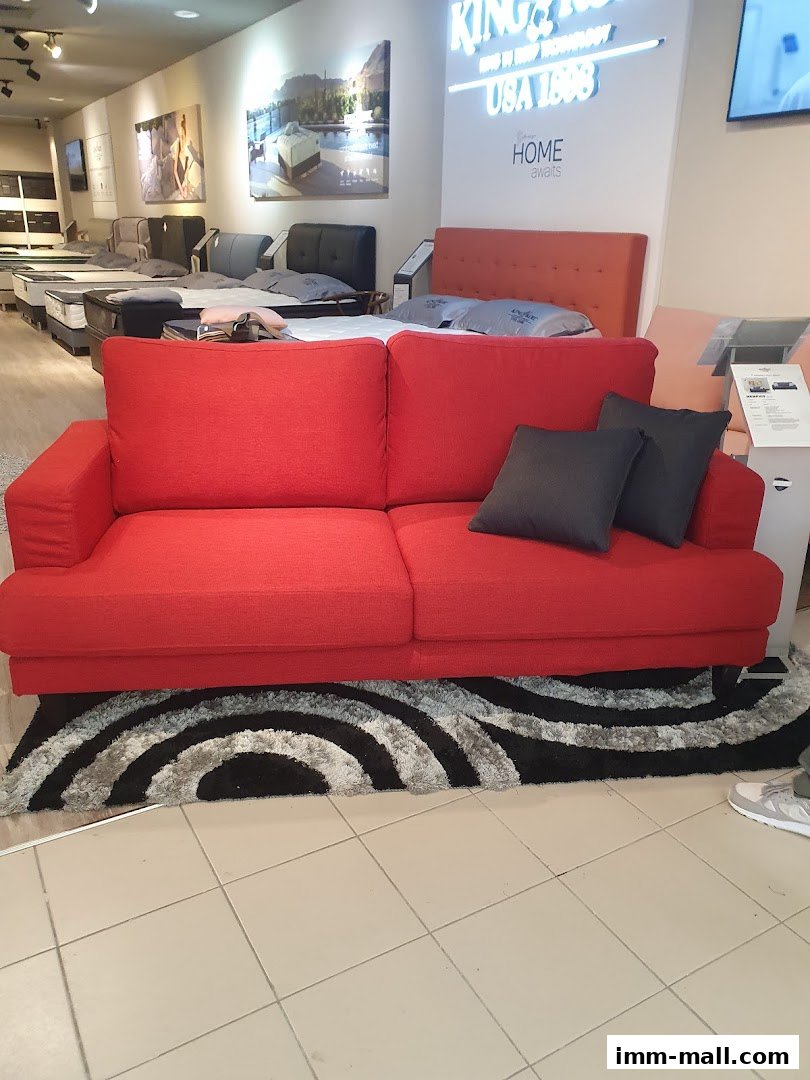 A bright red sofa with dark grey cushions is displayed in a furniture store showroom.