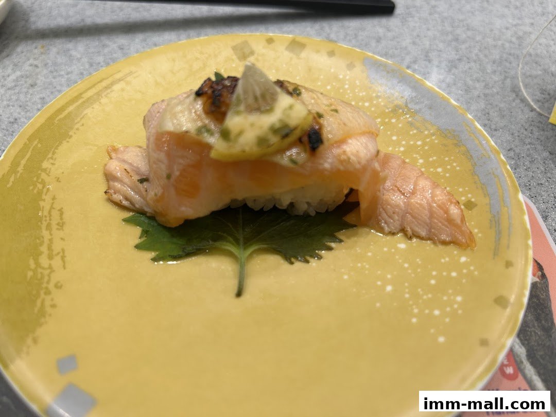 A close-up of a delicious salmon sushi dish on a yellow plate with a green leaf garnish.