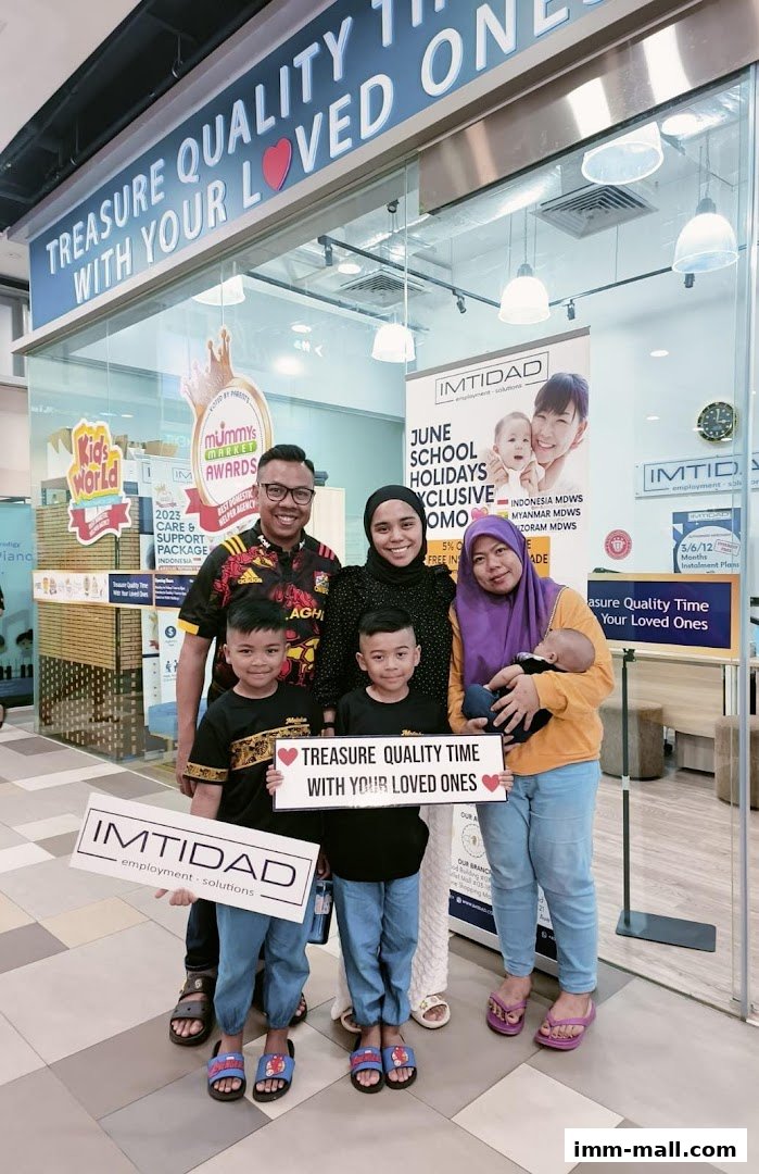 A family poses in front of the Imtidad Jurong IMM Branch, holding signs.