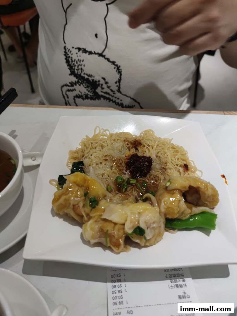 A plate of wonton noodles with a side of soup and a receipt.