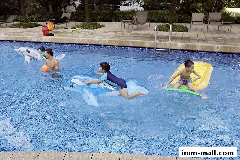 Children and an adult enjoy a sunny day at the pool with inflatable toys.