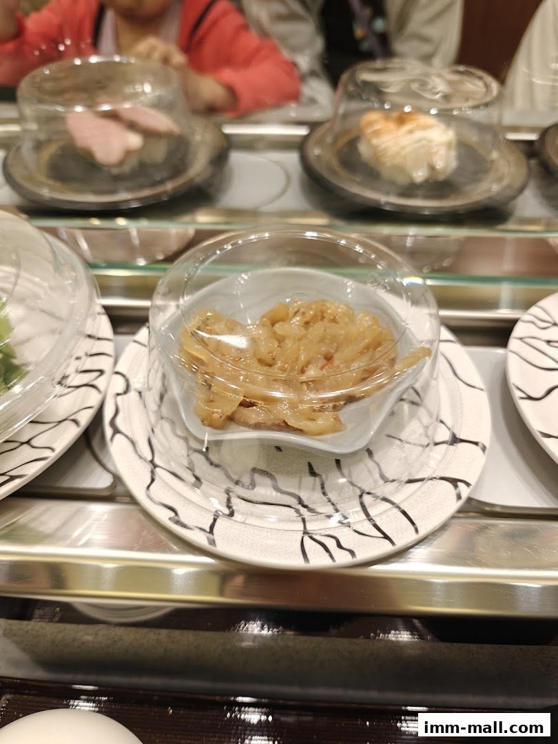 Sushi dishes on a conveyor belt at Sushi Express, with diners in the background.