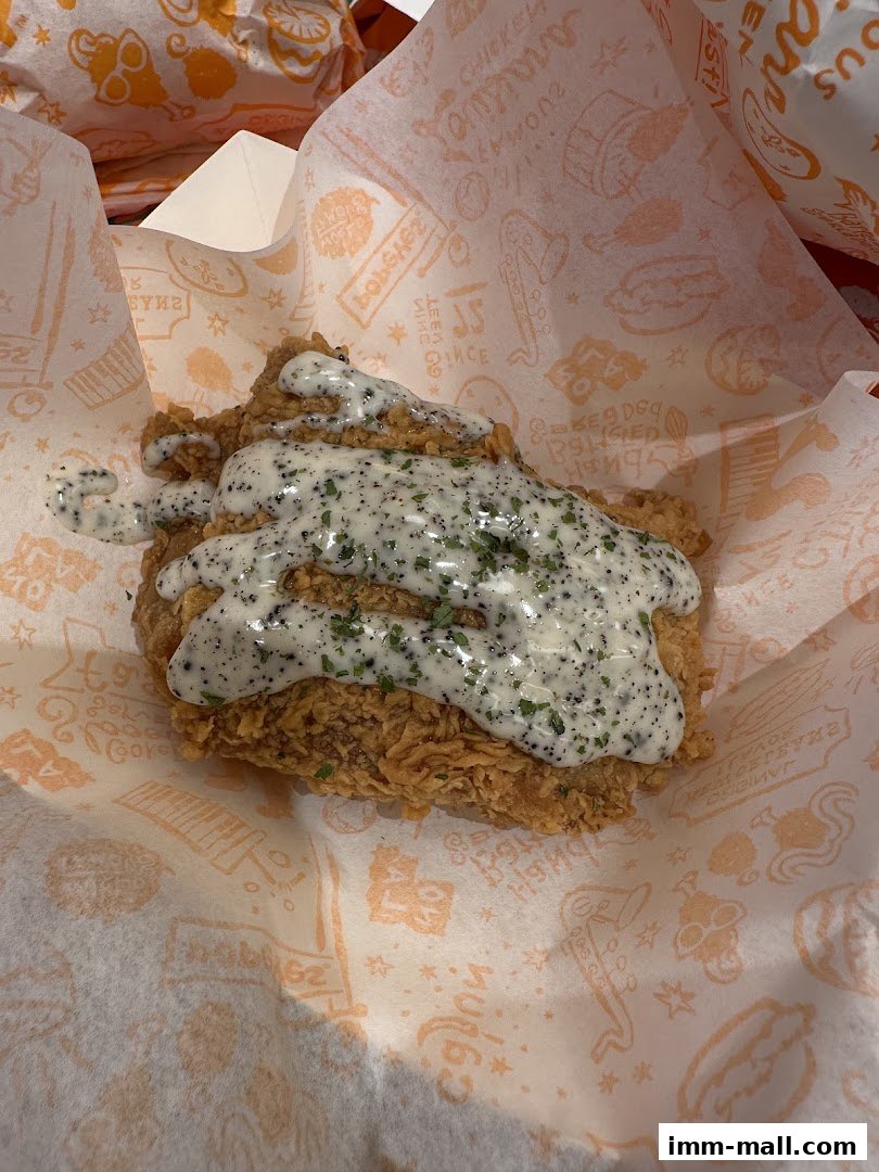 A piece of Popeyes fried chicken covered in creamy gravy and herbs.