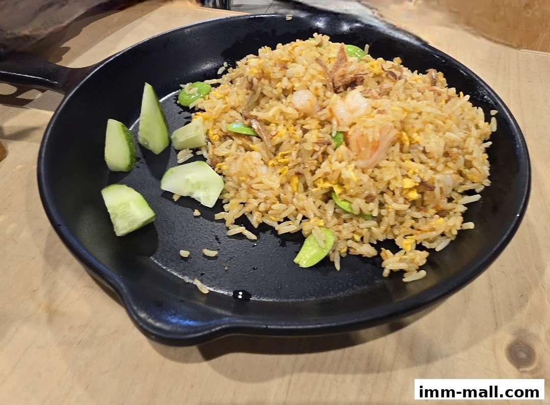 A plate of fried rice with shrimp and cucumber slices on a wooden table.