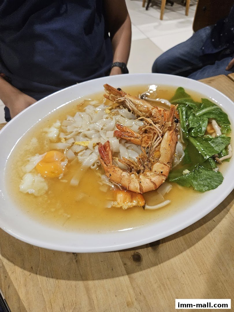 A close-up of a bowl of noodles with prawns, egg, and vegetables in broth.