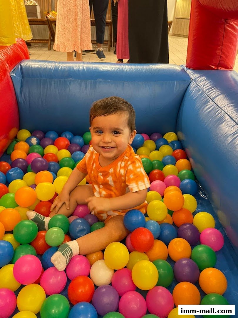A happy baby sits in a ball pit filled with colorful plastic balls.