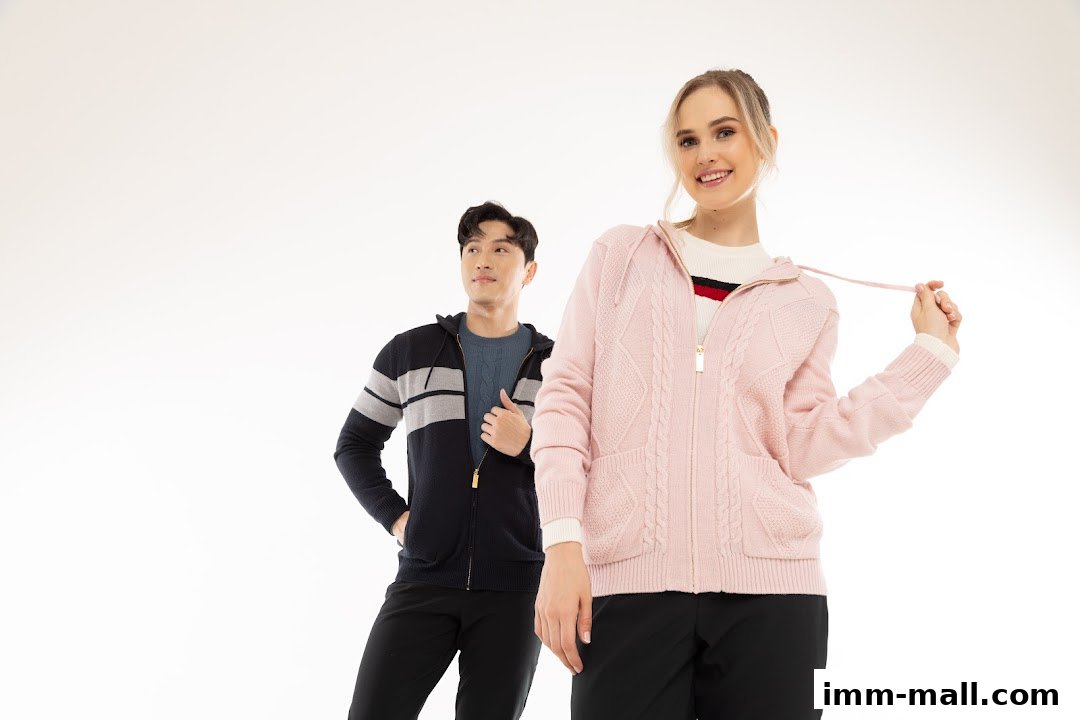 A woman in a pink cable-knit hoodie and a man in a striped hoodie stand against a white background.