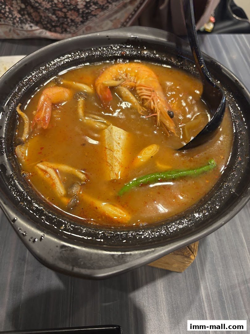 A steaming bowl of Tom Yum soup with shrimp, tofu, and mushrooms.