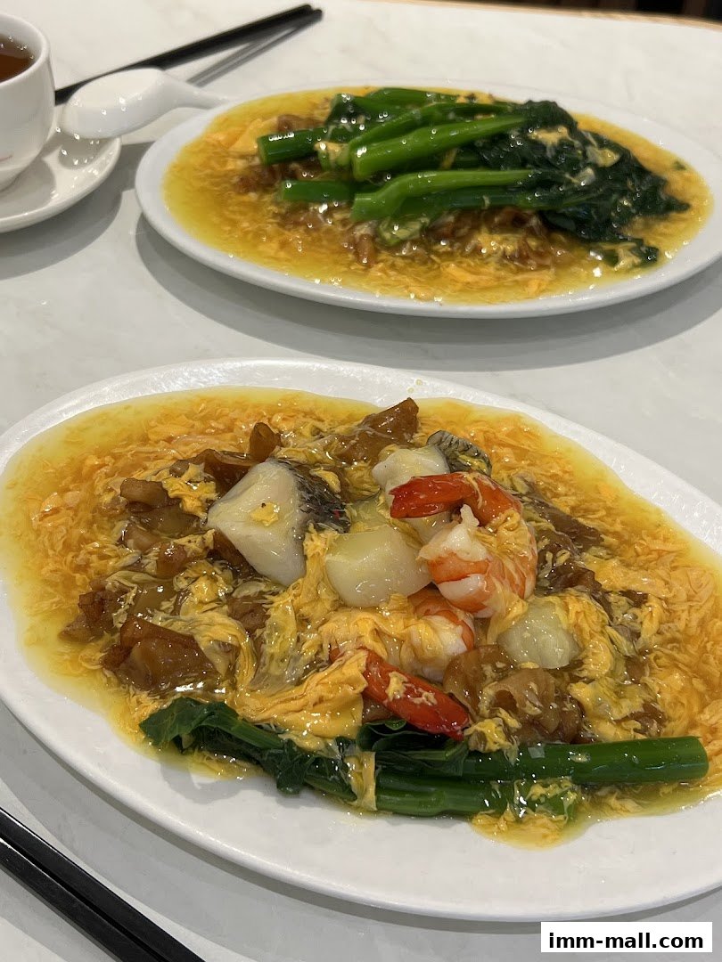 Two plates of Chinese food with vegetables, seafood, and scrambled egg sauce, served with tea.