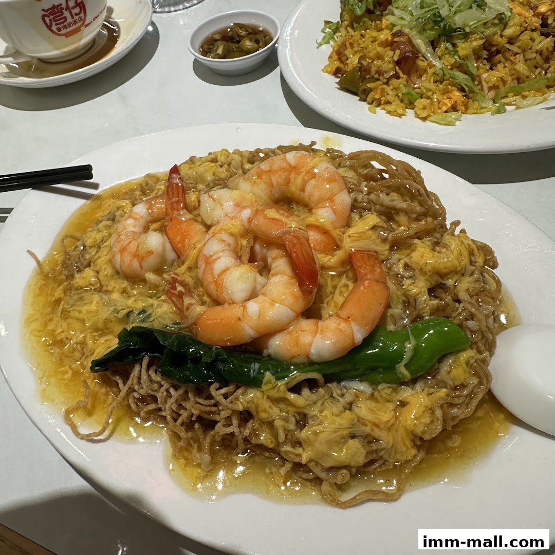 A plate of crispy noodles topped with shrimp and scrambled eggs, served with a side of fried rice.