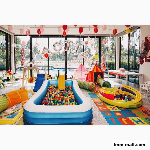 A vibrant indoor play area with a ball pit, slides, tunnels, and balloons.