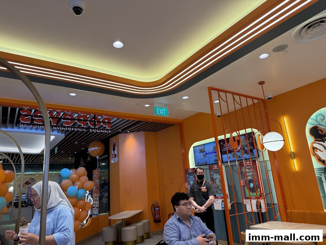Interior view of a Popeyes restaurant with customers and staff, featuring bright orange decor and balloons.