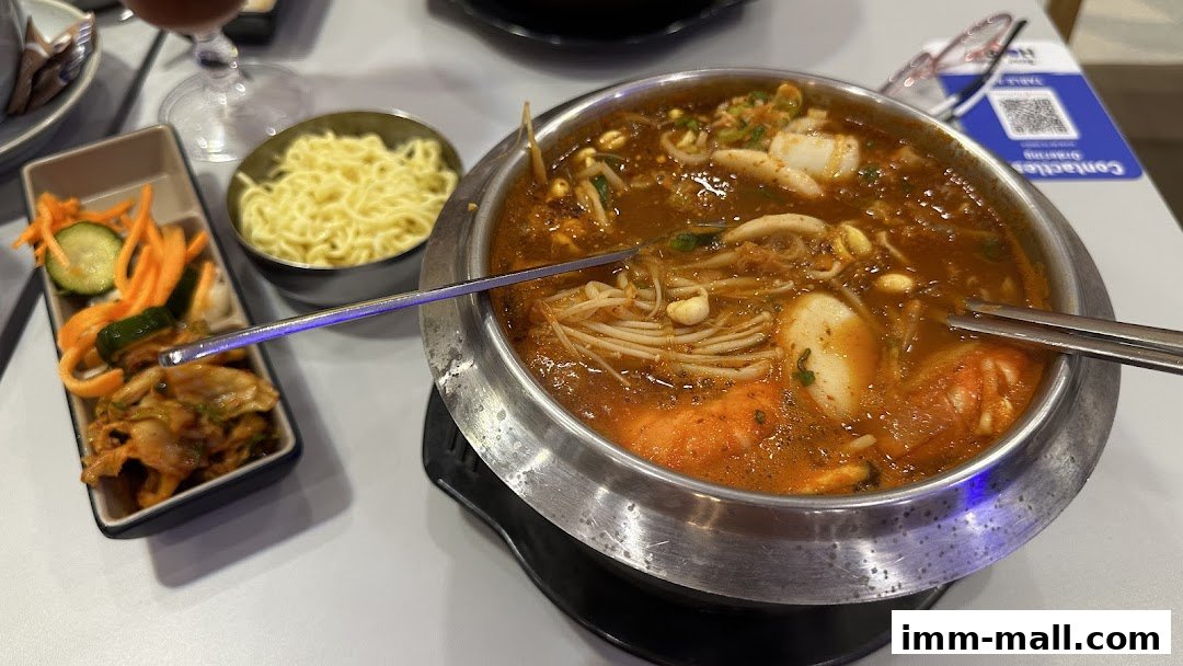 A steaming hotpot dish with noodles and kimchi side dishes.