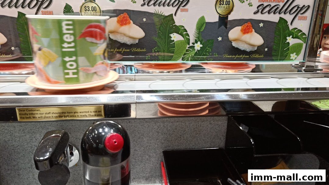 A conveyor belt sushi restaurant with a 'Hot Item' cup and Hokkaido scallop sushi displayed.