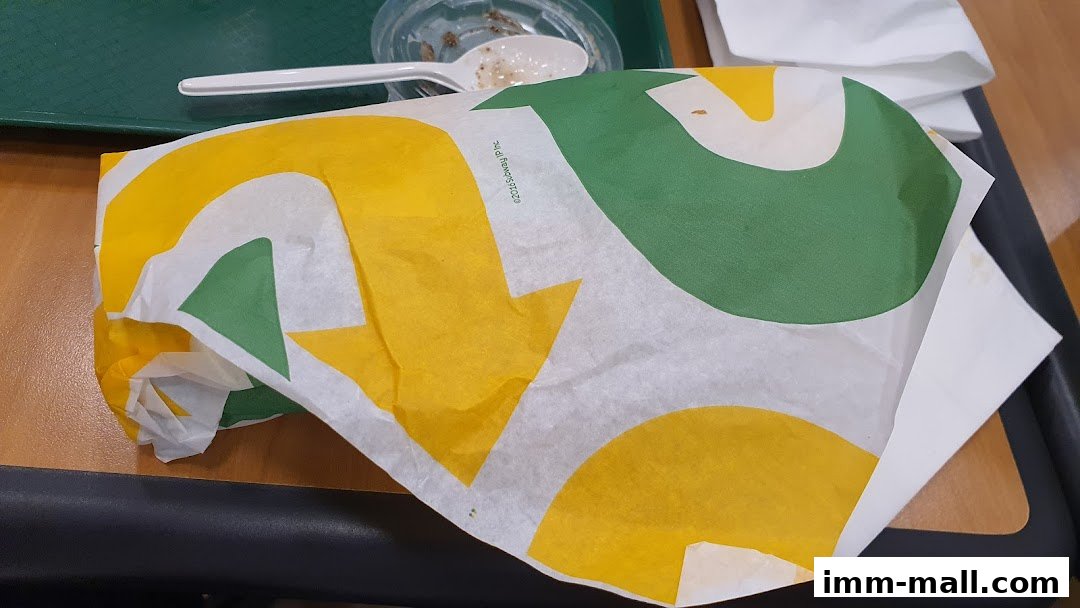 A Subway sandwich wrapped in branded paper on a tray with a plastic spoon and cup.