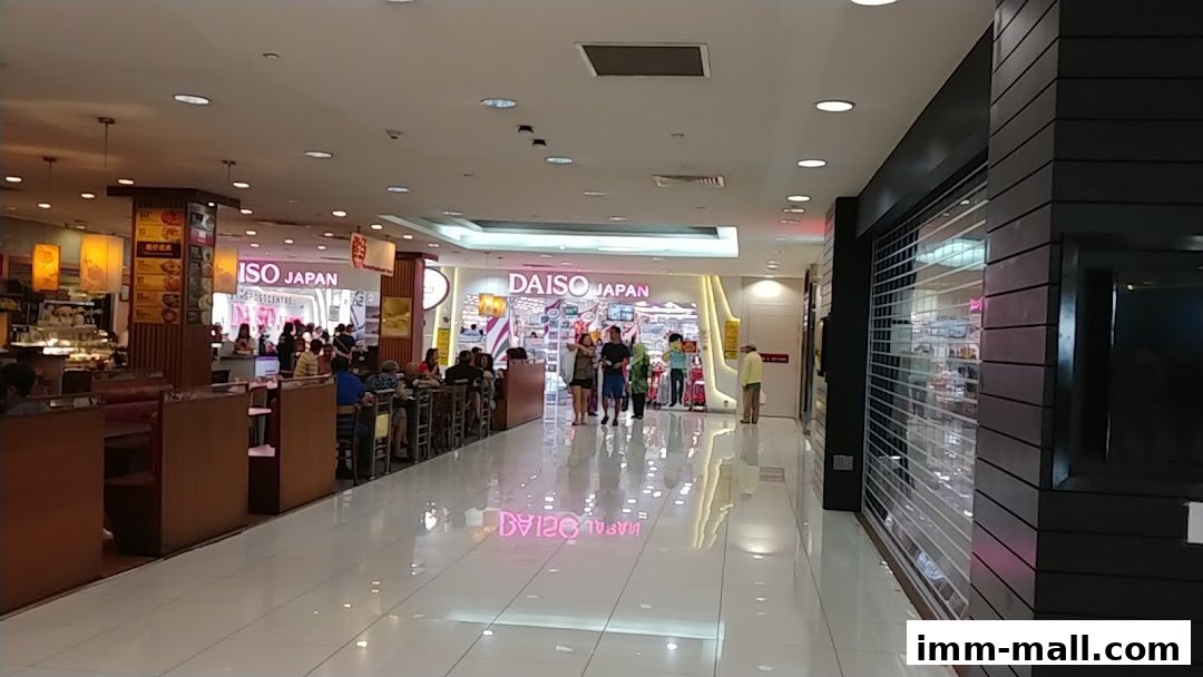 A bright shopping mall corridor with people walking past Daiso Japan stores.