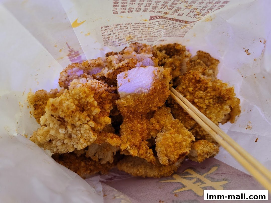 A close-up shot of crispy, seasoned fried chicken pieces in a paper bag with chopsticks.