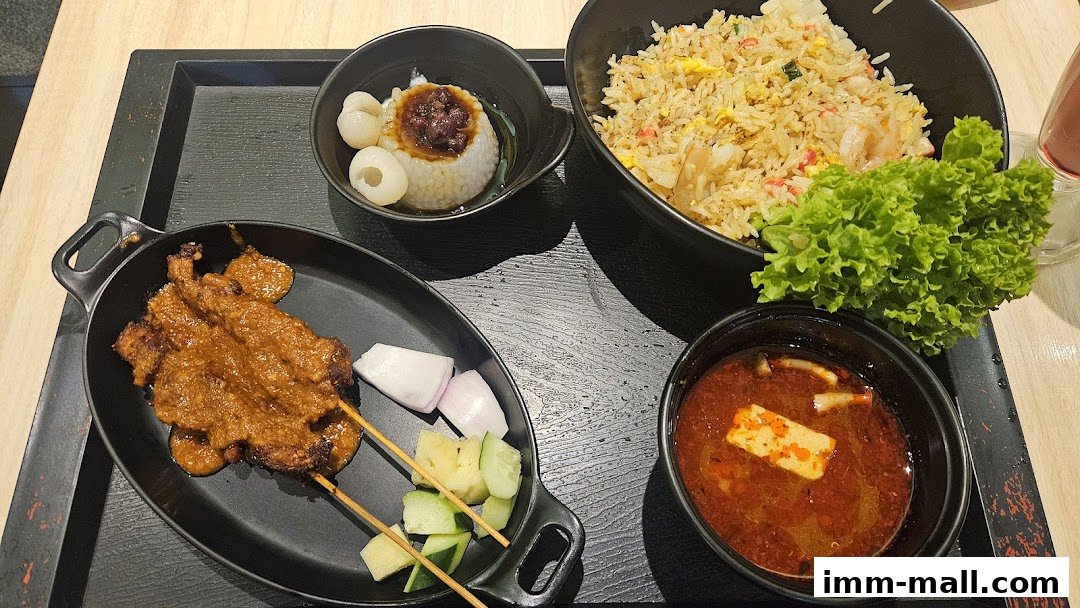 A tray of food featuring satay, fried rice, and a small bowl of soup with lychees.