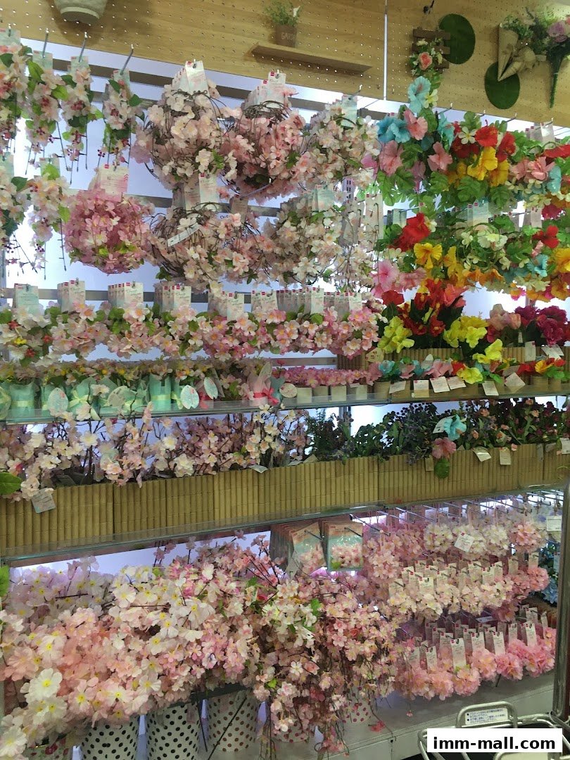 A vibrant display of artificial flowers, including cherry blossoms and hibiscus, arranged on shelves.