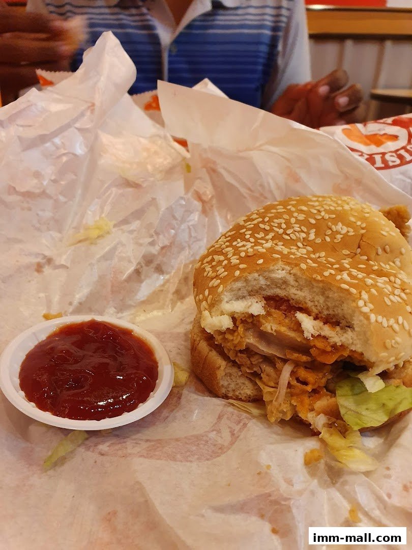 A partially eaten Popeyes chicken sandwich with a side of ketchup.