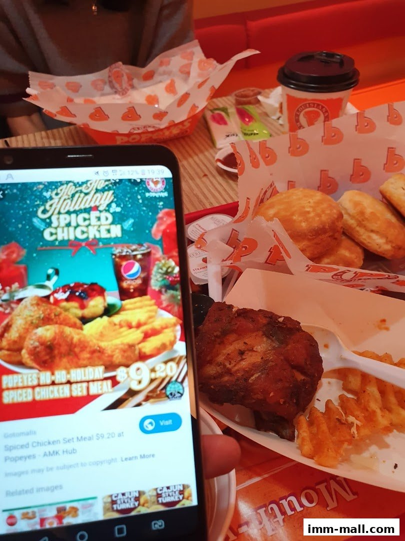 A phone displays a Popeyes holiday promotion next to a meal with fried chicken and fries.