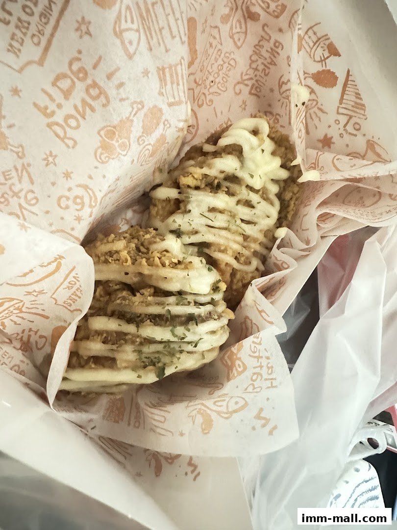 Close-up of crispy fried chicken pieces drizzled with white sauce and herbs.