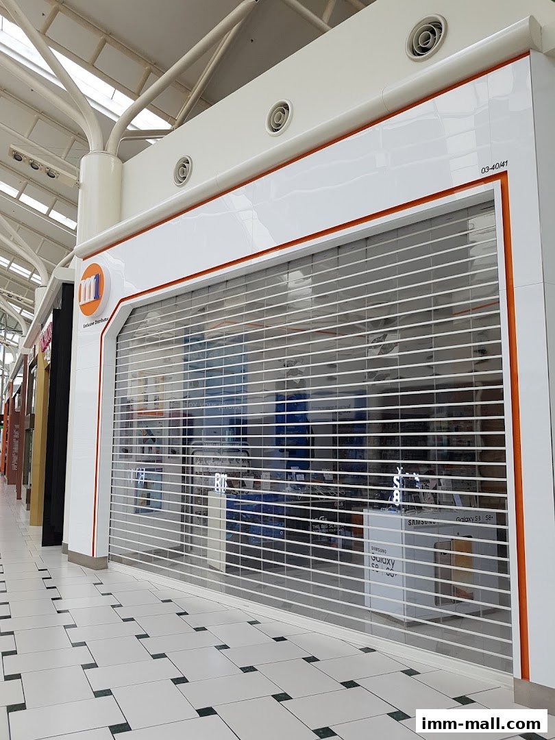 A closed phone shop with a security shutter, displaying Samsung Galaxy S8+ boxes inside.