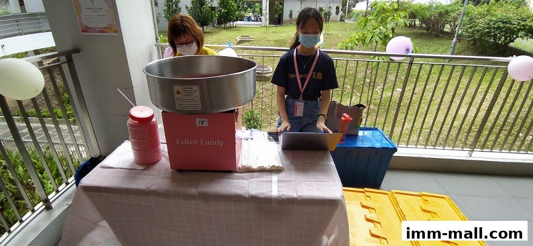 Two people operating a cotton candy machine at an outdoor event with balloons.