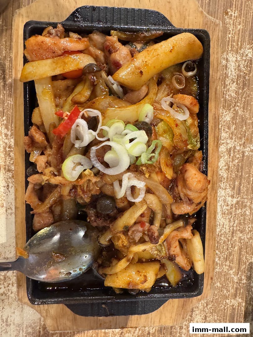 A sizzling hot pot dish with chicken, rice cakes, and vegetables served in a cast iron pan.