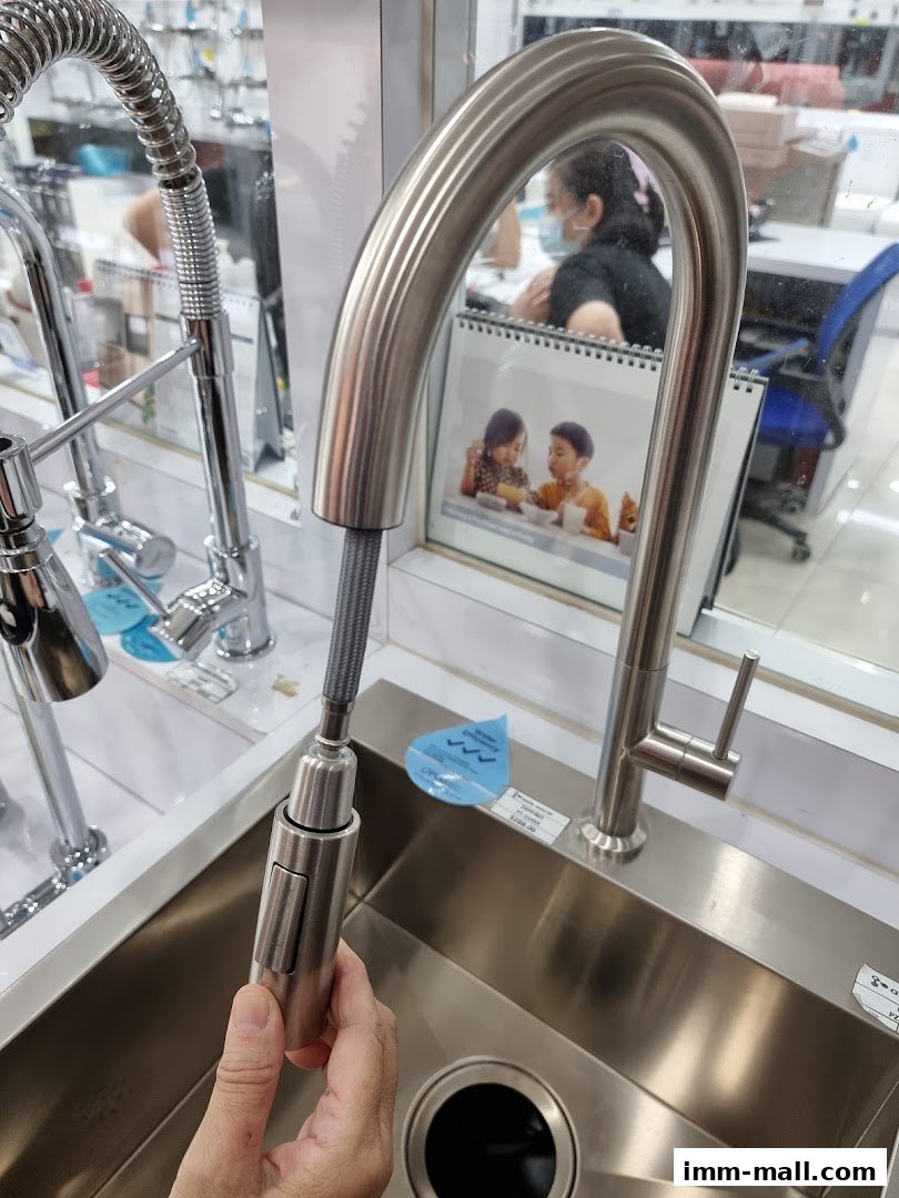 A person is holding a modern kitchen faucet over a stainless steel sink.