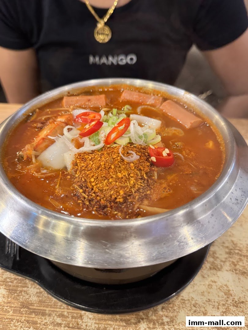 A steaming bowl of Korean stew with hot dogs, chili, and scallions.