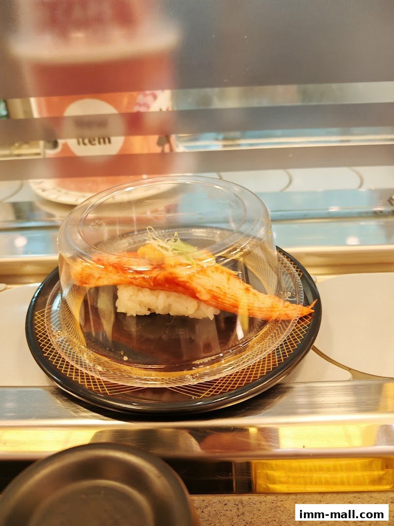 A close-up of a sushi item with crab stick on a conveyor belt.