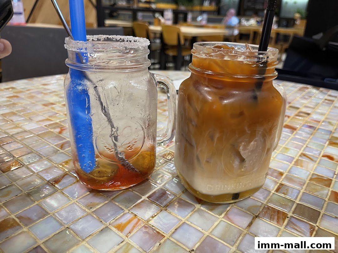 Two refreshing drinks, one iced coffee and one soda with fruit, served in mason jars on a tiled table.