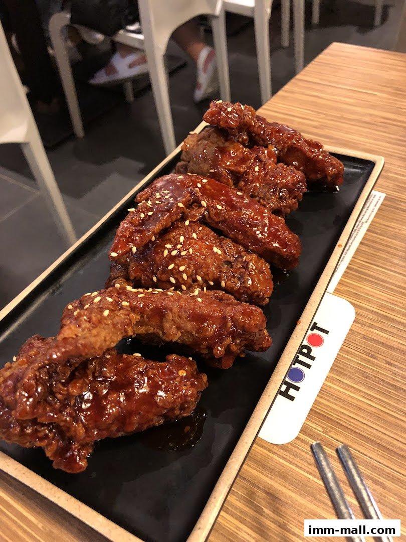 A plate of glistening Korean fried chicken wings with sesame seeds on a black platter.
