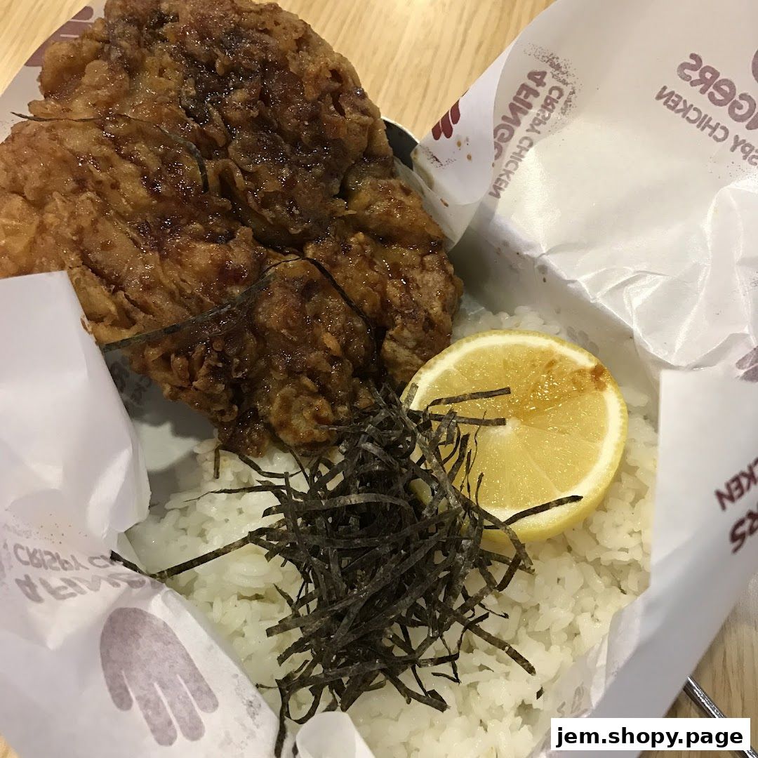 A close-up of crispy fried chicken with rice, seaweed, and a lemon slice.